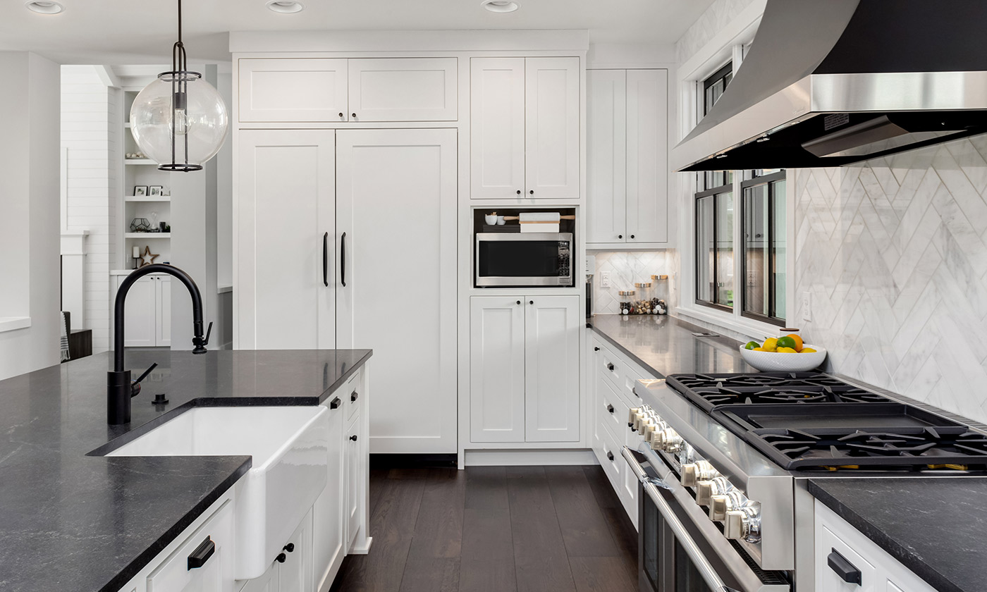 Modern kitchen with black countertops, white cabinets, wooden floors, and black hardware